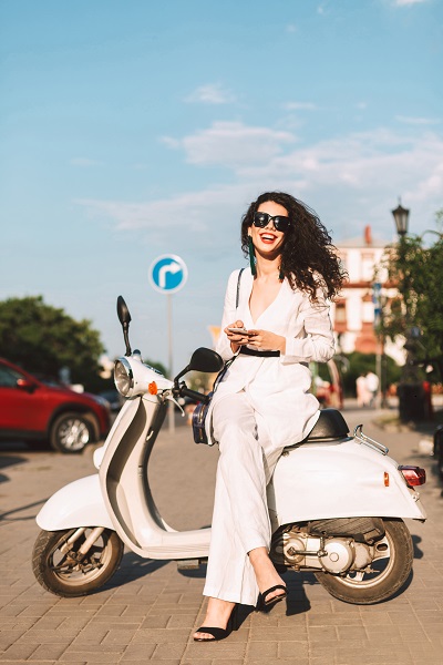 ﻿Smiling Ukrainian lady in a suit and sunglasses sitting on a moped happily looking in a camera